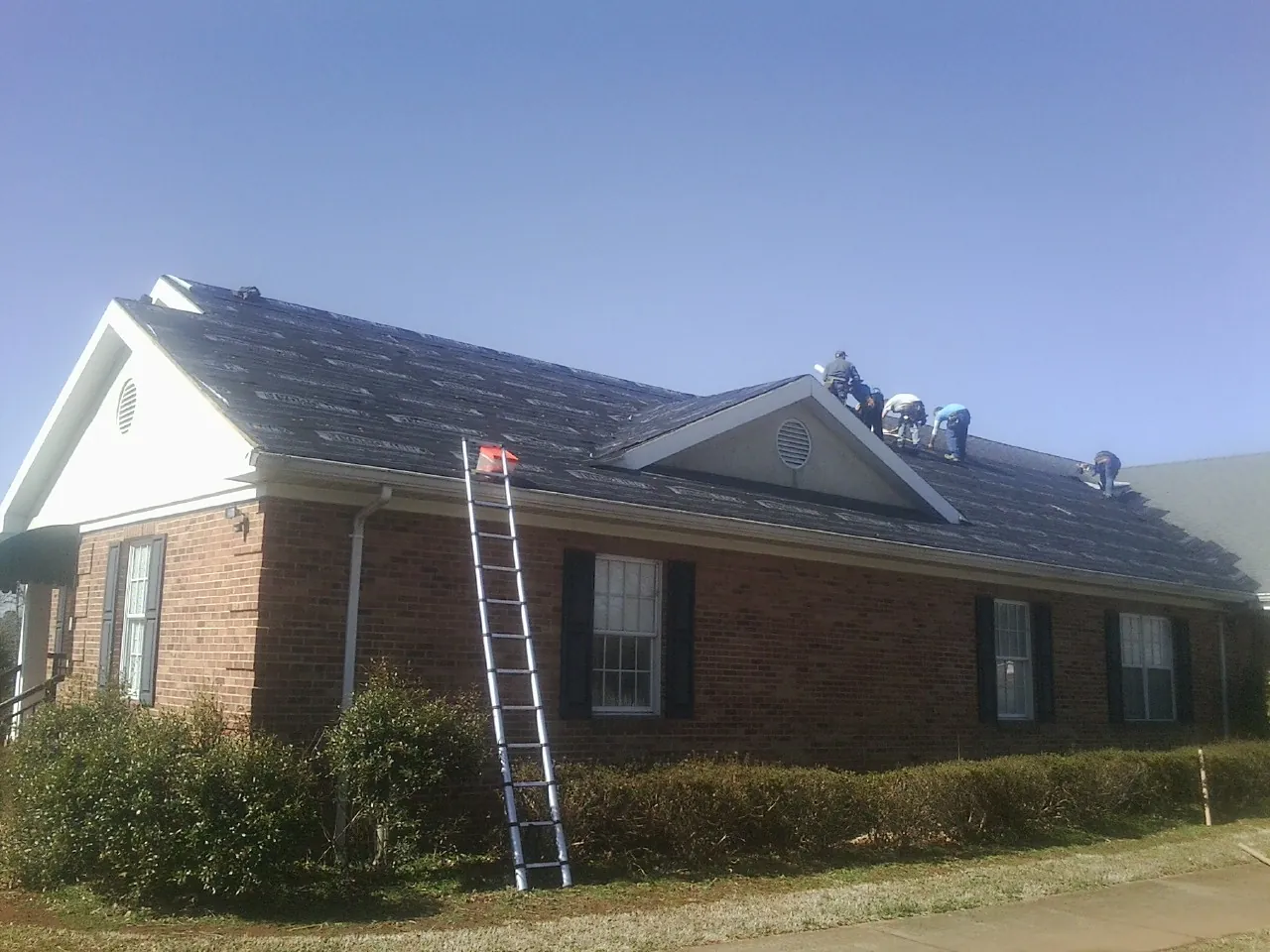 Crew tearing shingles off a brick ranch roof with a ladder set — Metal Roof Repair work by our crew in Pentwater