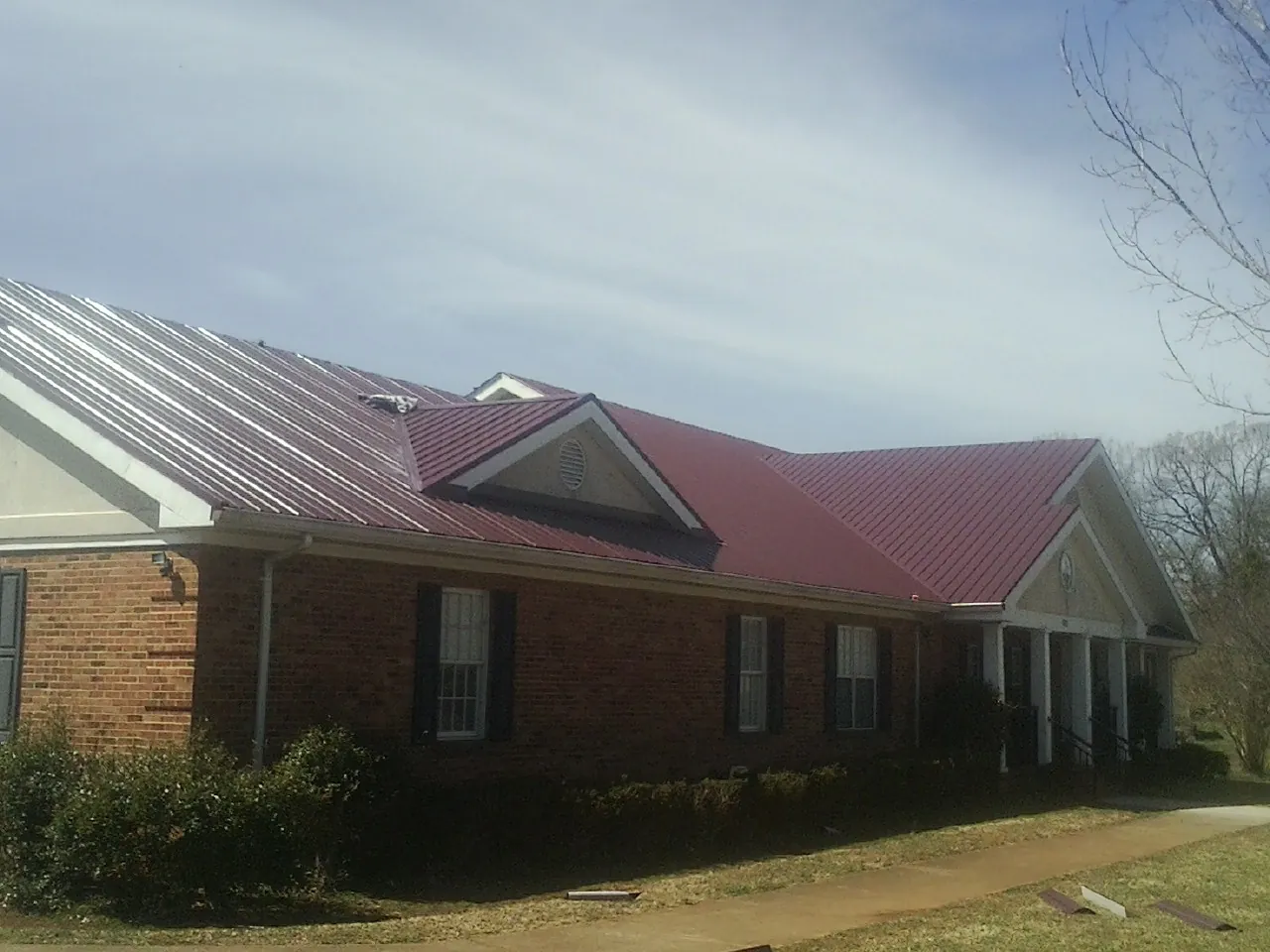 Red metal roof with gabled entries on a long brick building, from a Hail Damage Roof Repair job in Pentwater