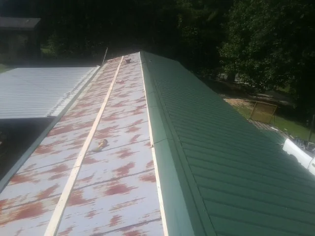 Old rusted panels beside newly installed green metal roofing — Wind Damage Roof Repair by Roofing Brothers in Pentwater