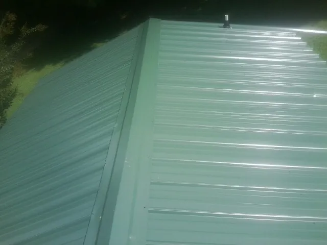 New green metal panels meeting at the ridge of a roof — Flat Roof Repair work by our crew in Pentwater