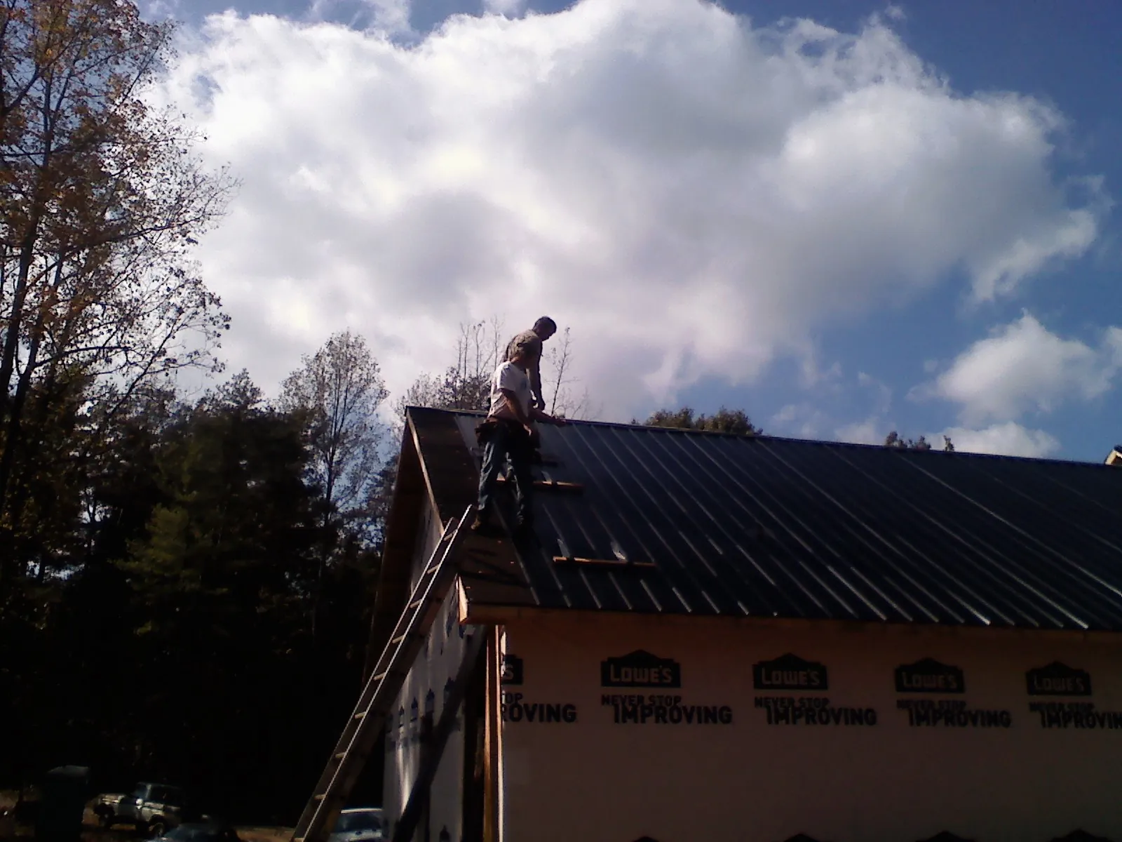 Roofer fastening dark metal panels high against a cloudy sky, from a Roof Inspection job in Pentwater