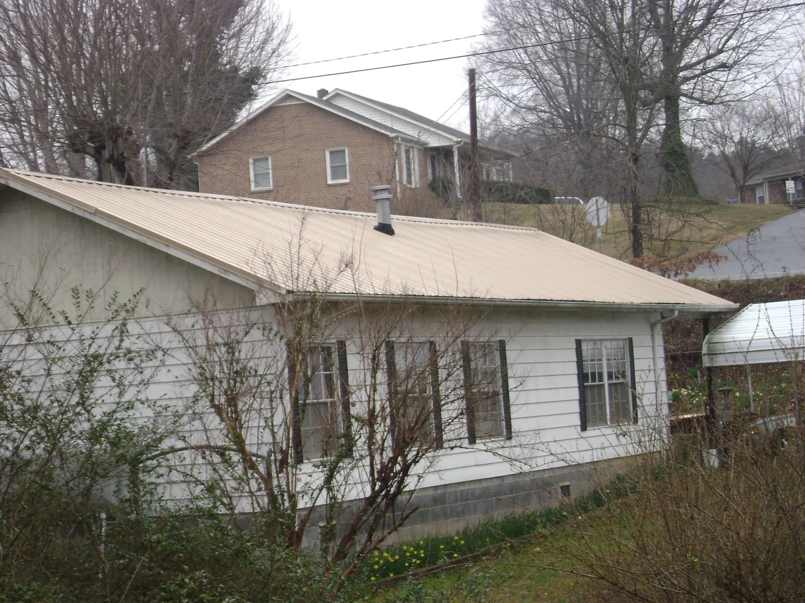 Tan metal roof on a white sided house set into a hillside — Commercial Roofing by Roofing Brothers in Pentwater