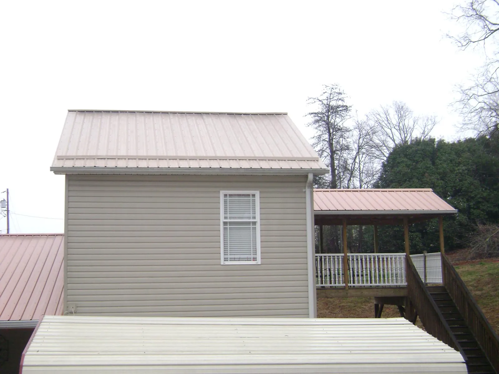 Tan metal roofs on a two story addition and attached porch, from a Roof Replacement job in Pentwater